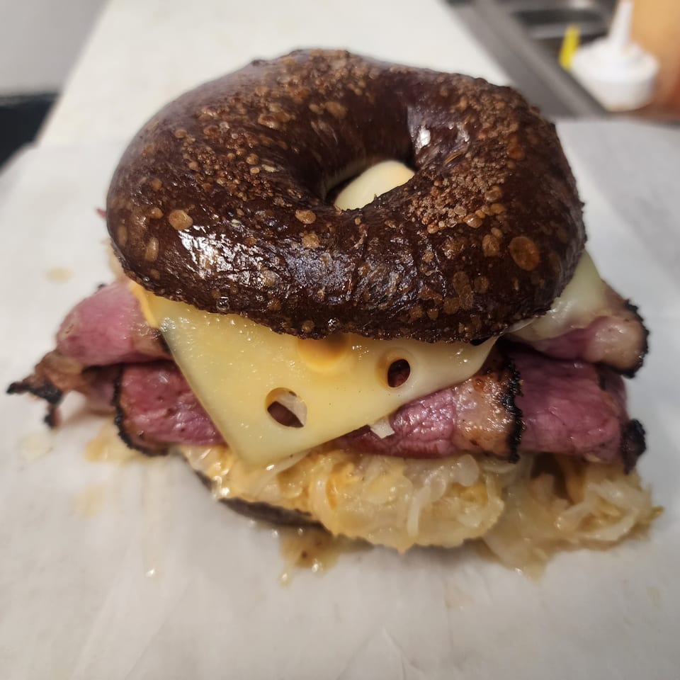 Dark bagel sandwich with pastrami, Swiss cheese, and sauerkraut on white paper.