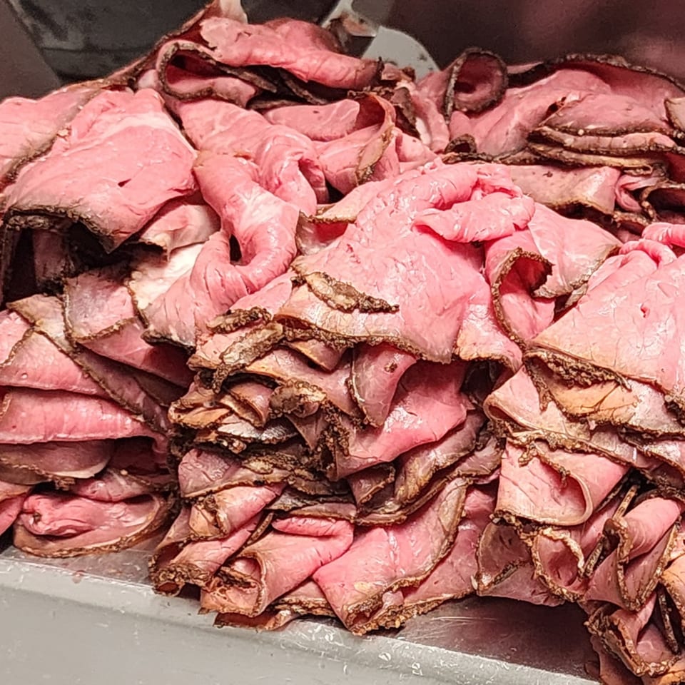 Piles of thinly sliced, pink roast beef with dark, seasoned edges, ready for sandwiches.