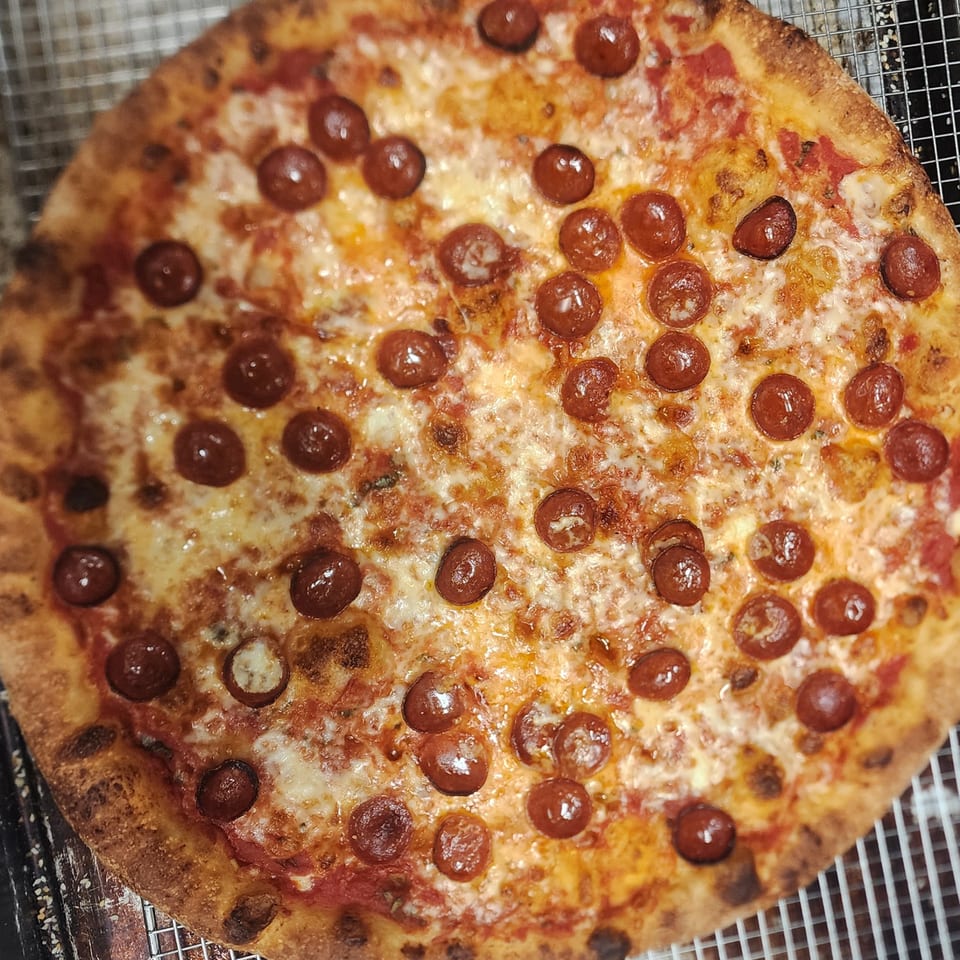 A freshly baked pepperoni pizza with melted cheese and a crispy crust on a cooling rack.